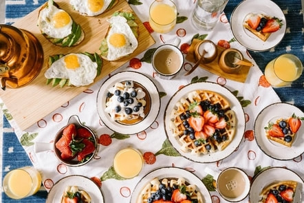 Picture of plates with different breakfast foods, including waffles with whipped cream and berries, eggs, and orange juice.