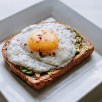 Picture of avocado toast with fried egg on top, on a fancy square plate.